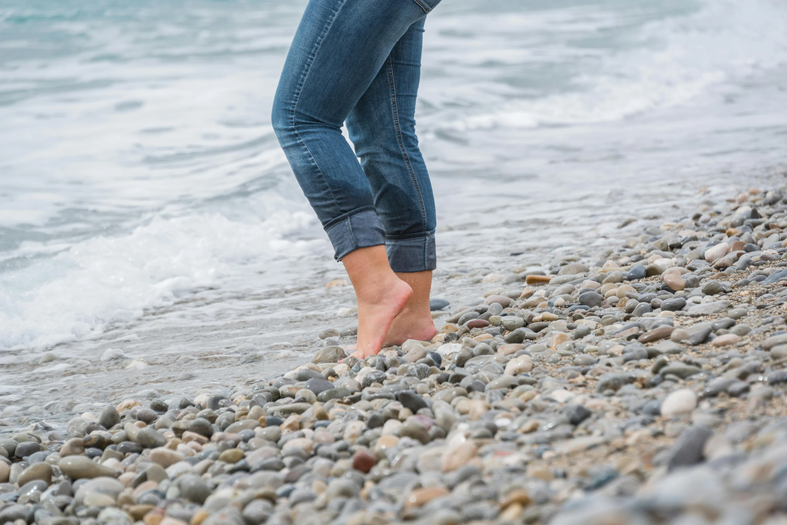 Person standing barefoot on shore with stones